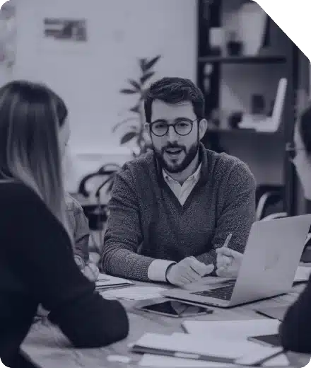 h1-mask1 A group of professionals engaged in a discussion around a laptop and documents on a wooden table.