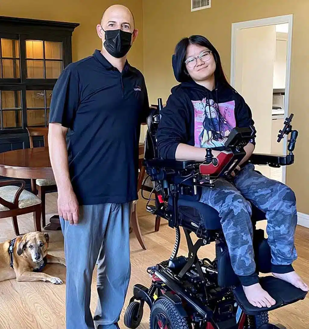 ilevel A person in a power wheelchair is smiling next to a standing man wearing a mask.